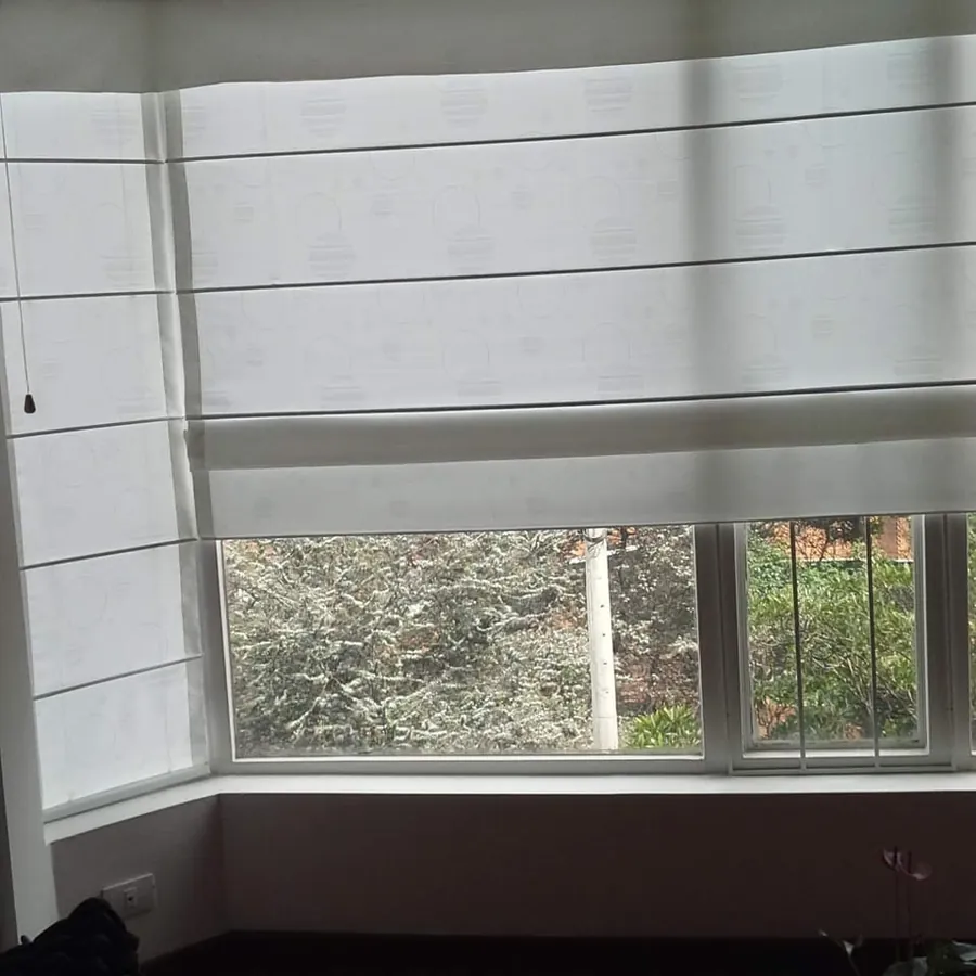 Cortinas romanas blancas instaladas a la medida en una ventana en L