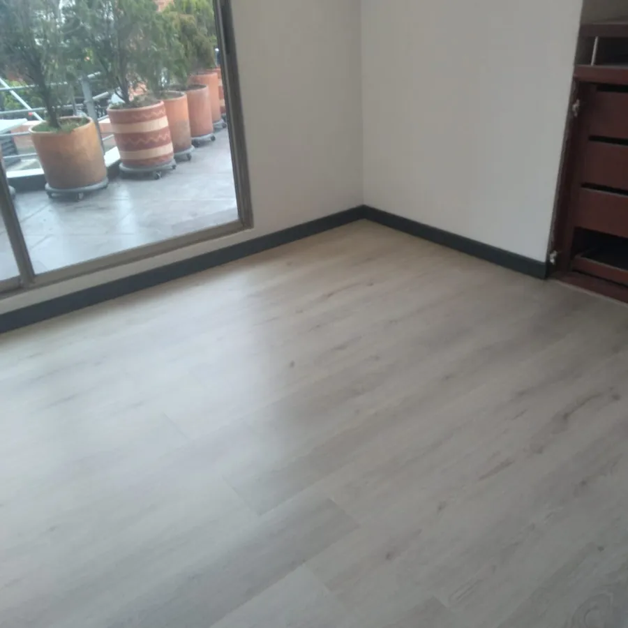 Sala con piso laminado en tono claro instalado junto al ventanal del balcón